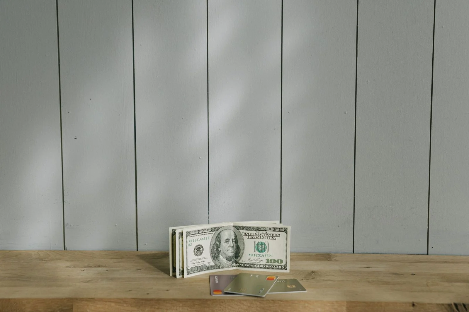 Pila de billetes de cien dólares y tarjetas de crédito sobre una superficie de madera.