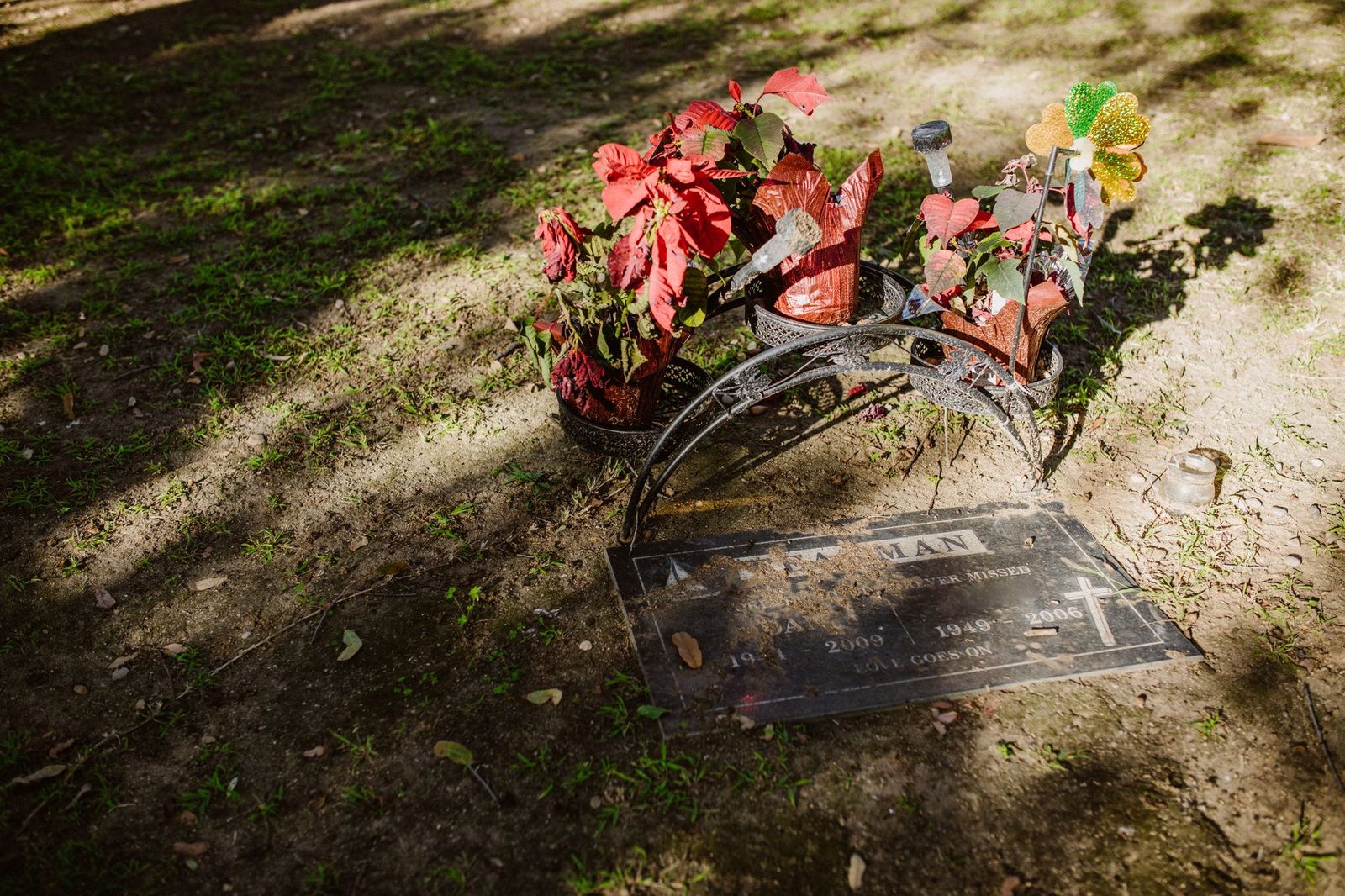 Sunlit grave decorated with bright red flowers and metal ornaments.