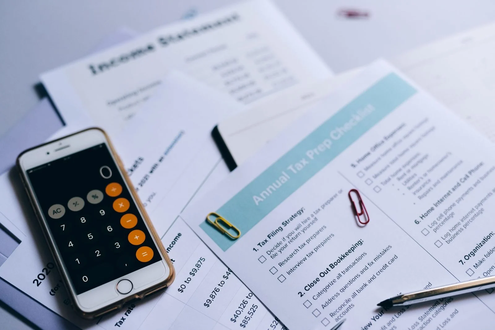 Tax preparation documents, a smartphone calculator, and a checklist laid out on a desk.