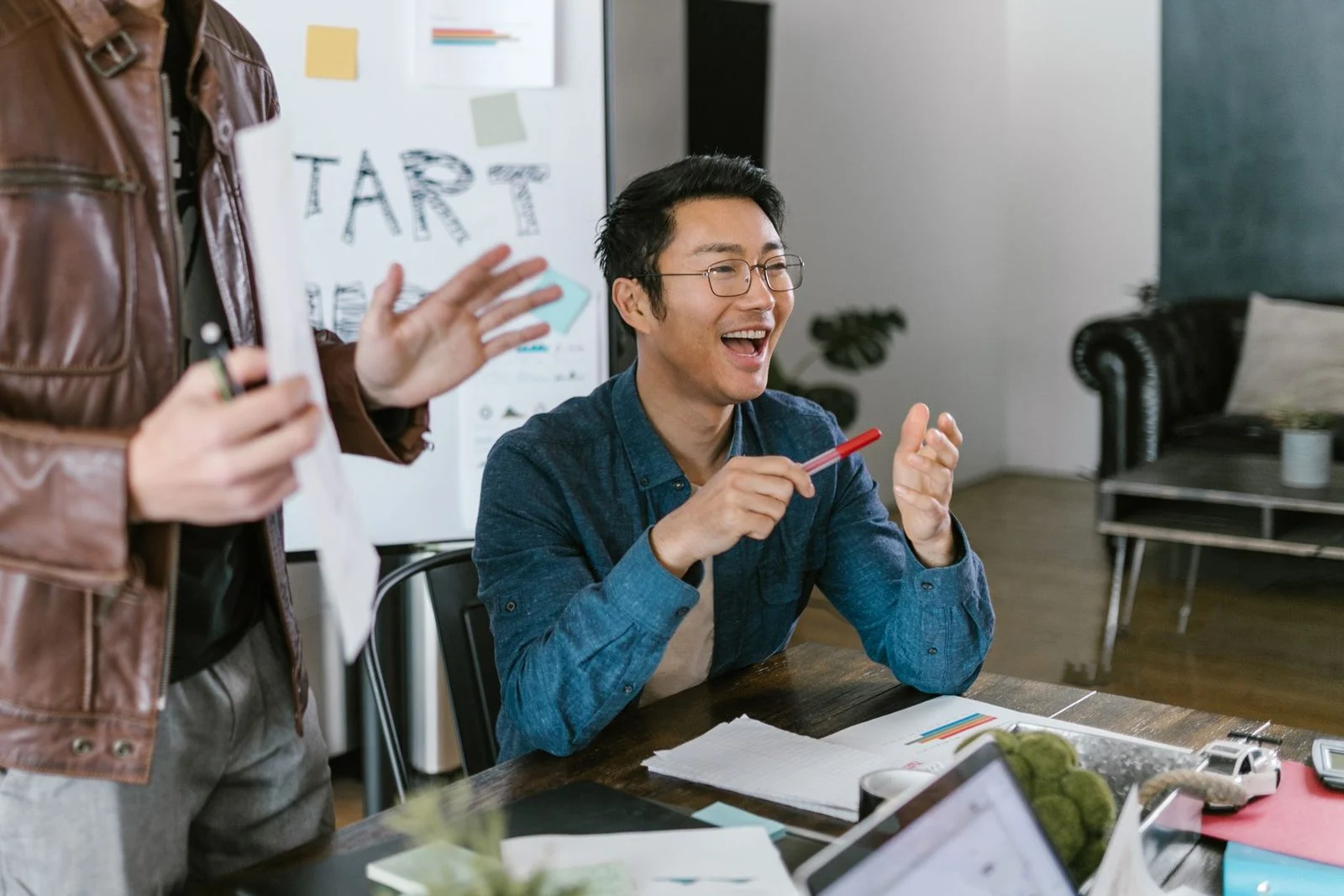 Team members in a lively office meeting discuss startup ideas and innovation around a table.