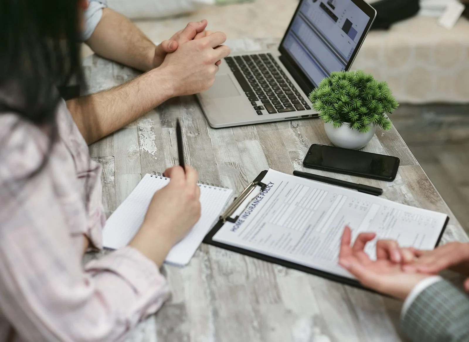 Two colleagues review a home insurance policy on a laptop, with notes spread across an office desk.