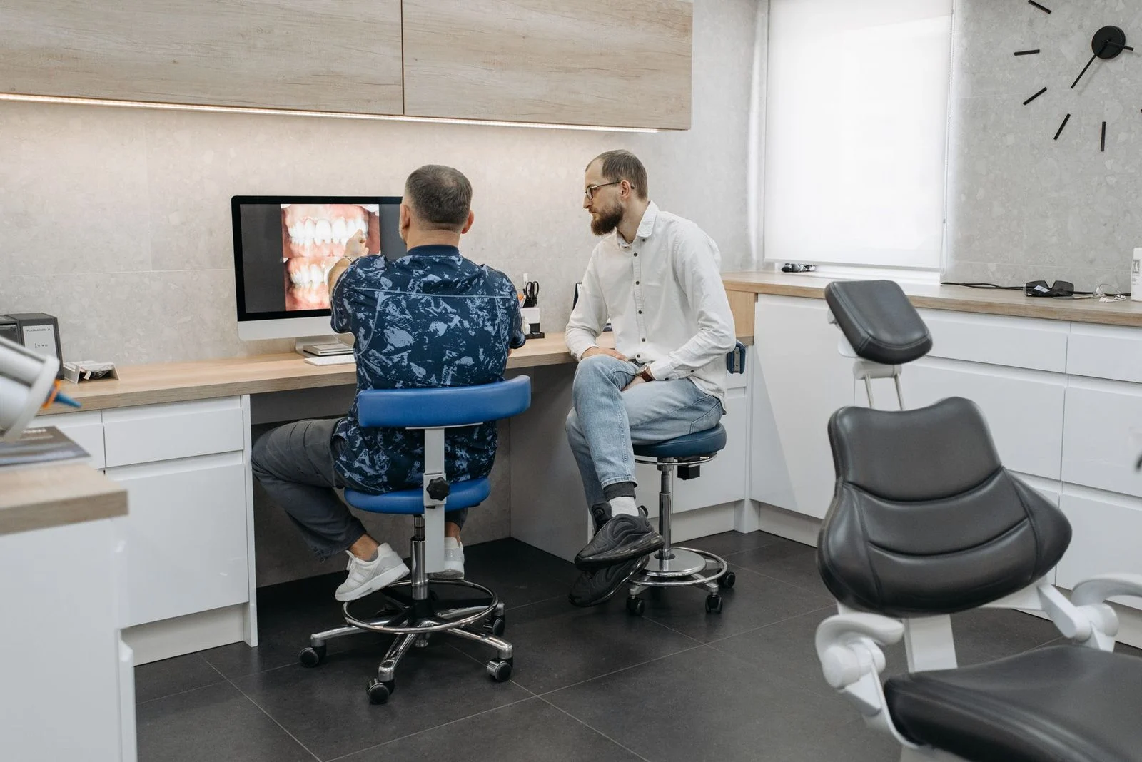 Dos profesionales dentales revisan juntos una radiografía dental en una pantalla dentro de una clínica moderna.
