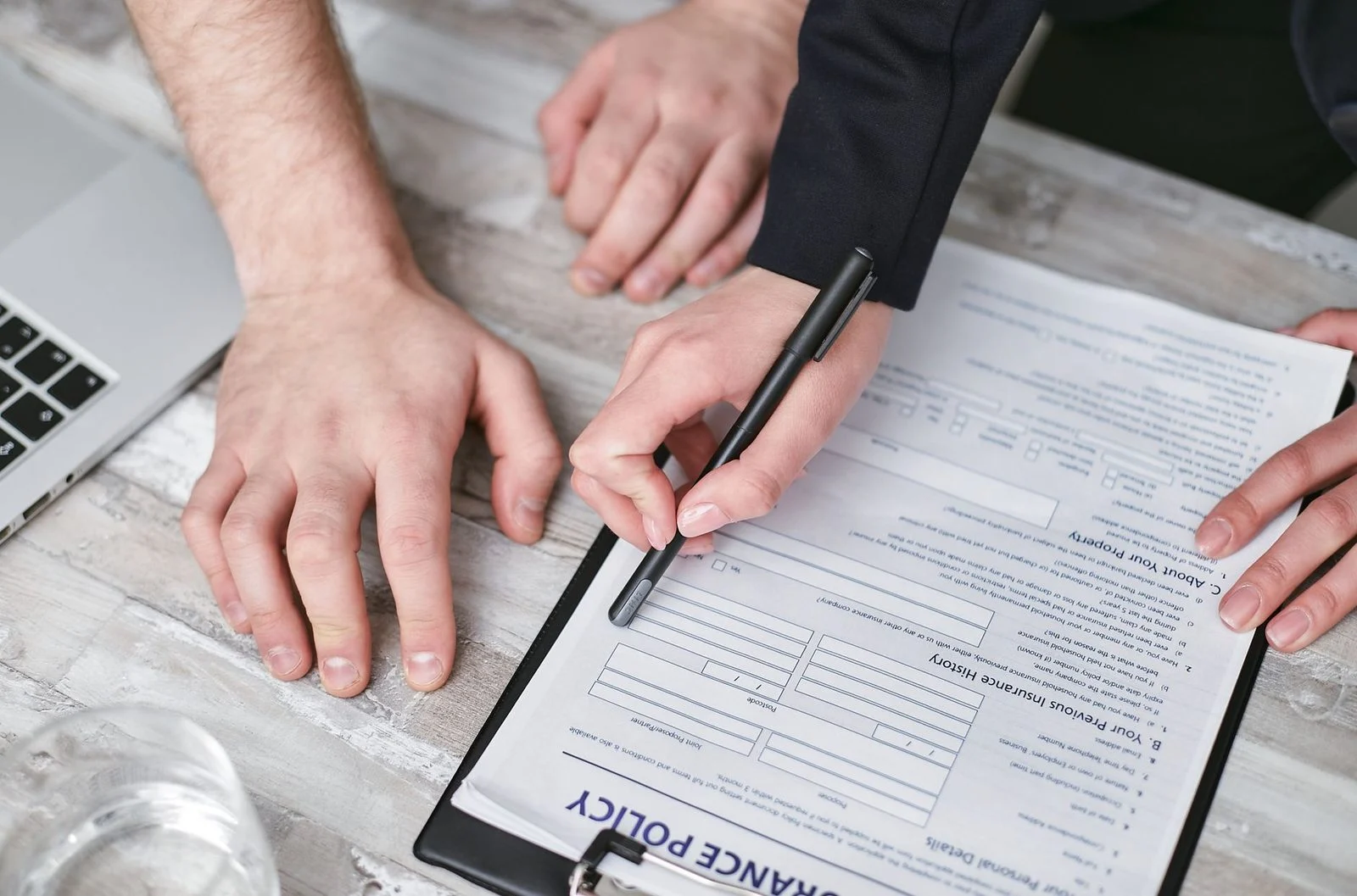 Two people sign an insurance policy document on a wooden desk.