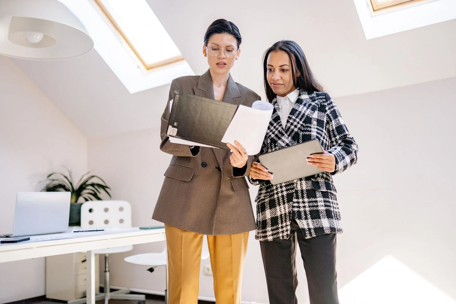 Two professionals reviewing business documents at a desk in a modern office.