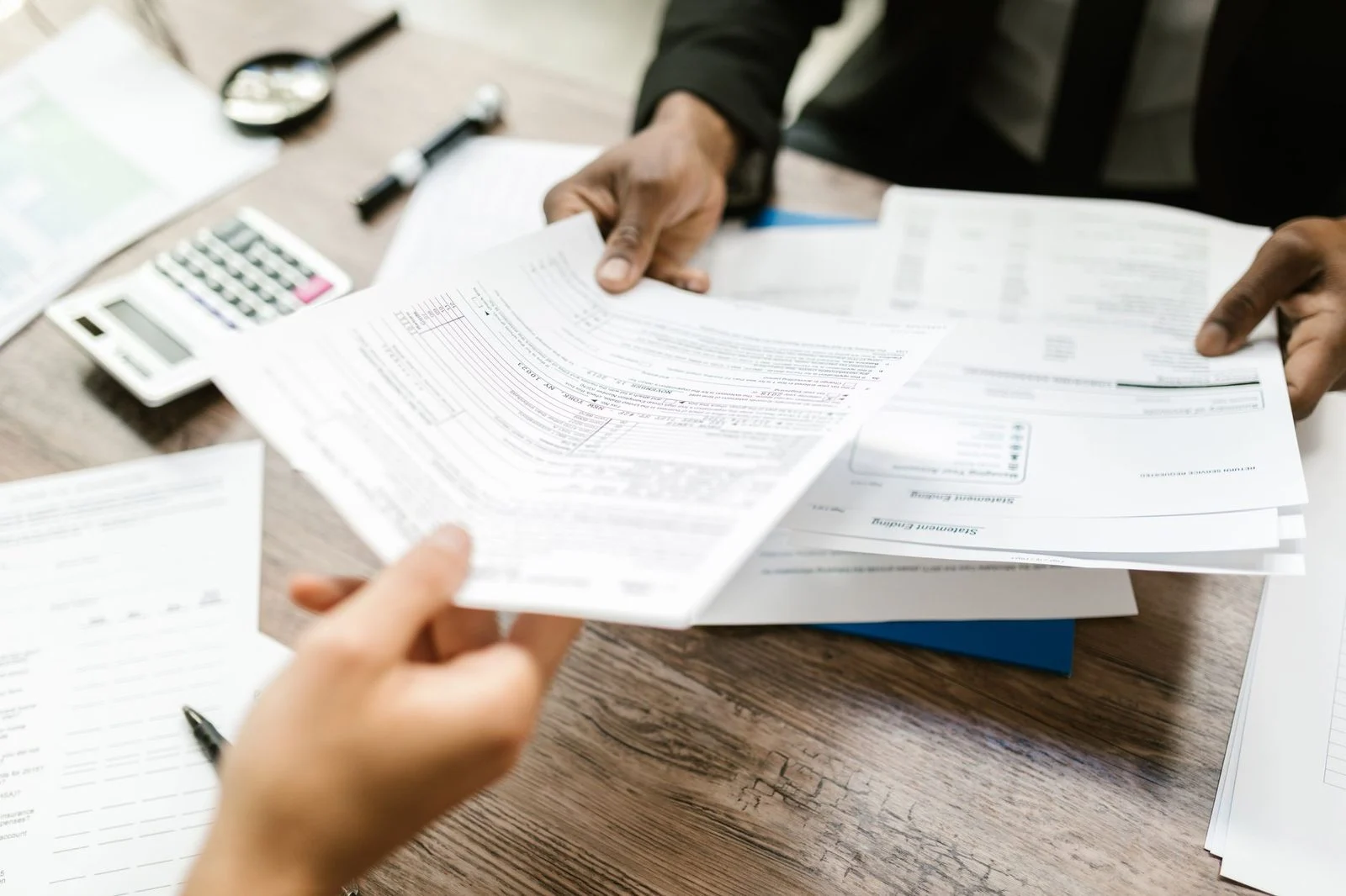 Two professionals sit together at a desk, reviewing documents and financial data in a bright office.