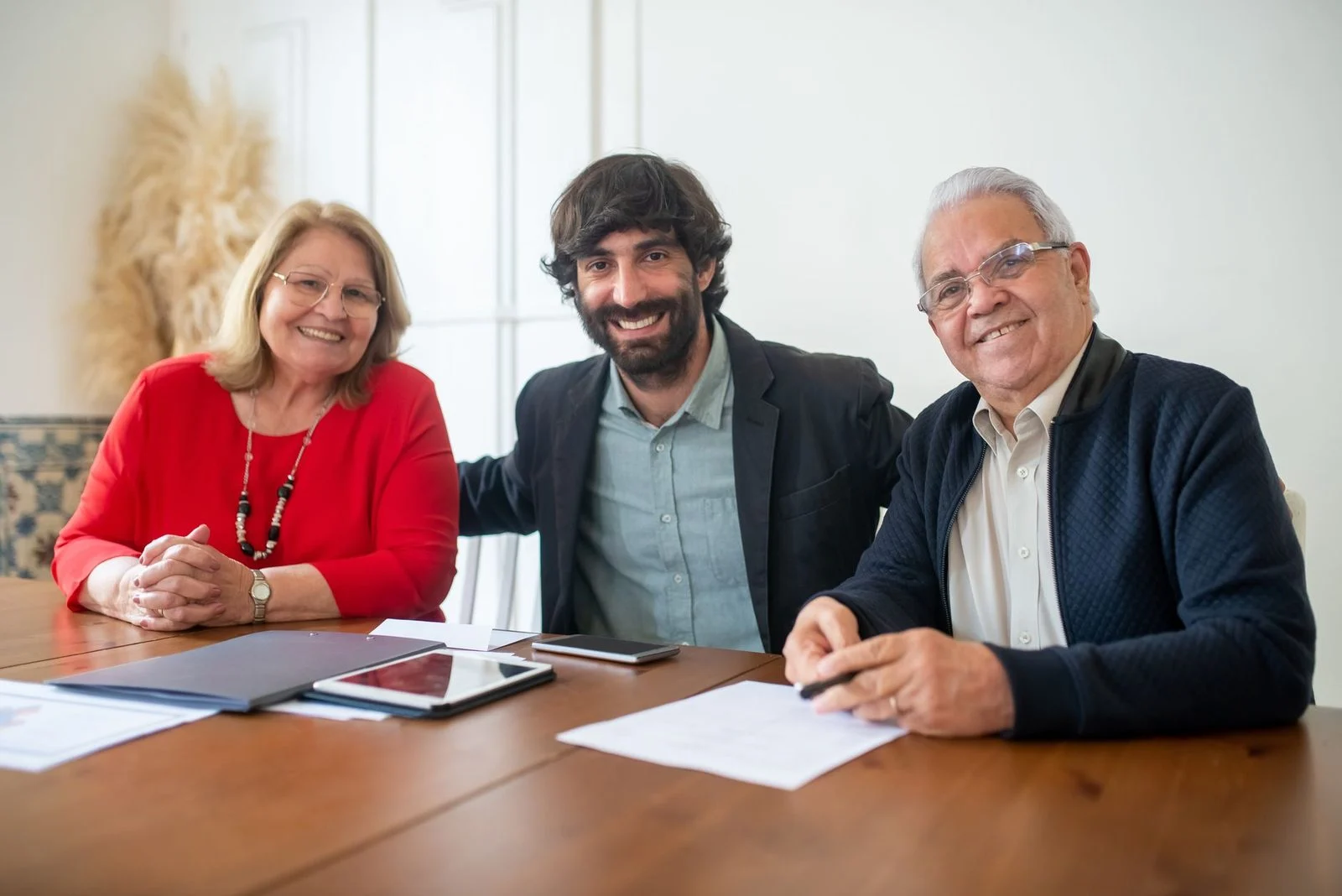Two senior adults and a young man smile together at an indoor business meeting.