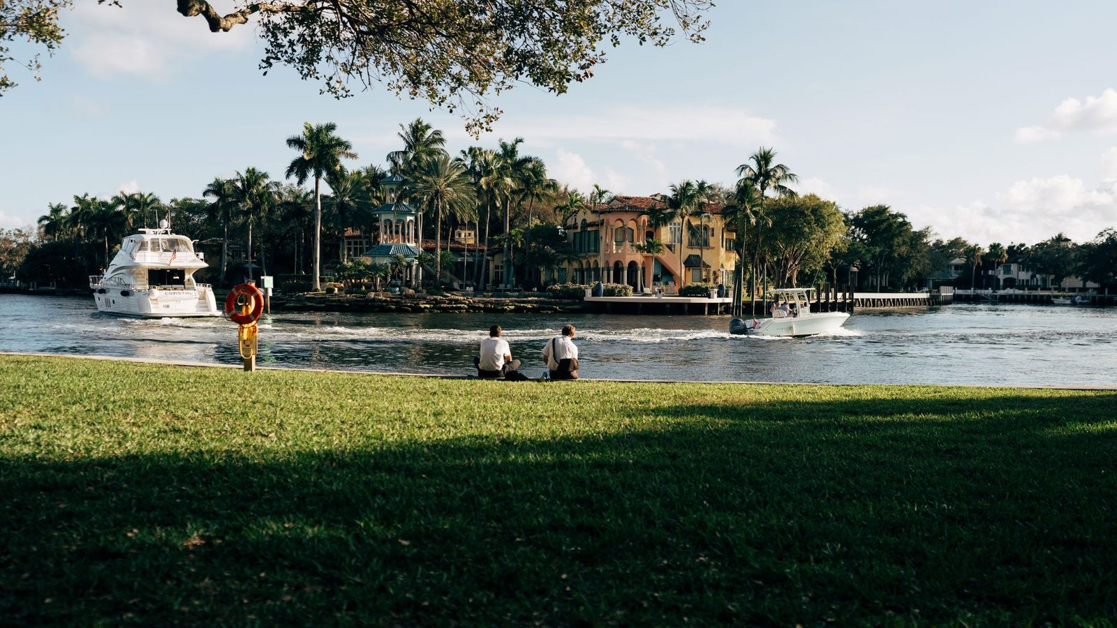 Vista tranquila del río con palmeras, botes y personas descansando junto al agua en Fort Lauderdale.