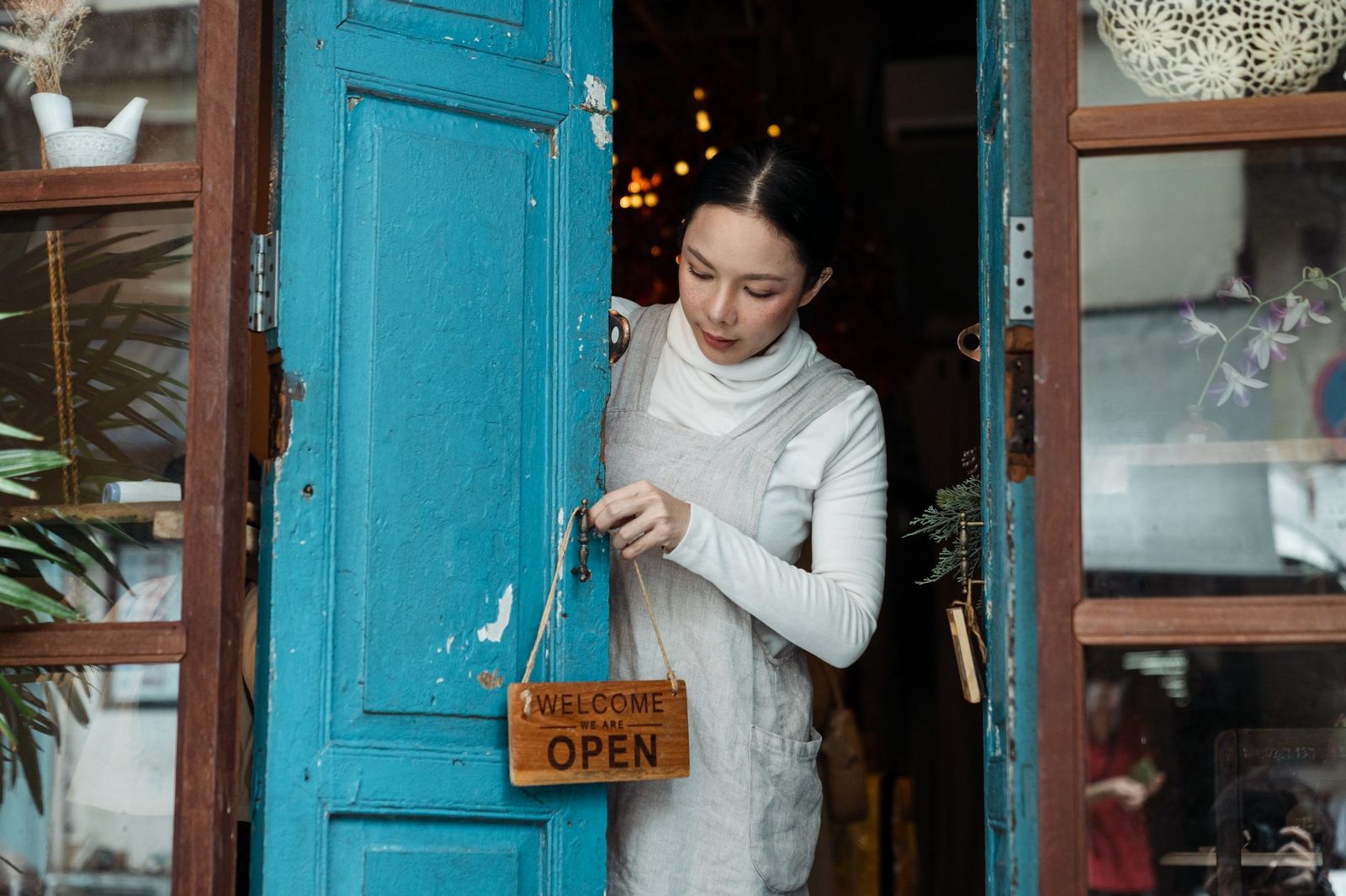 Woman hanging an open sign on a blue cafe door.