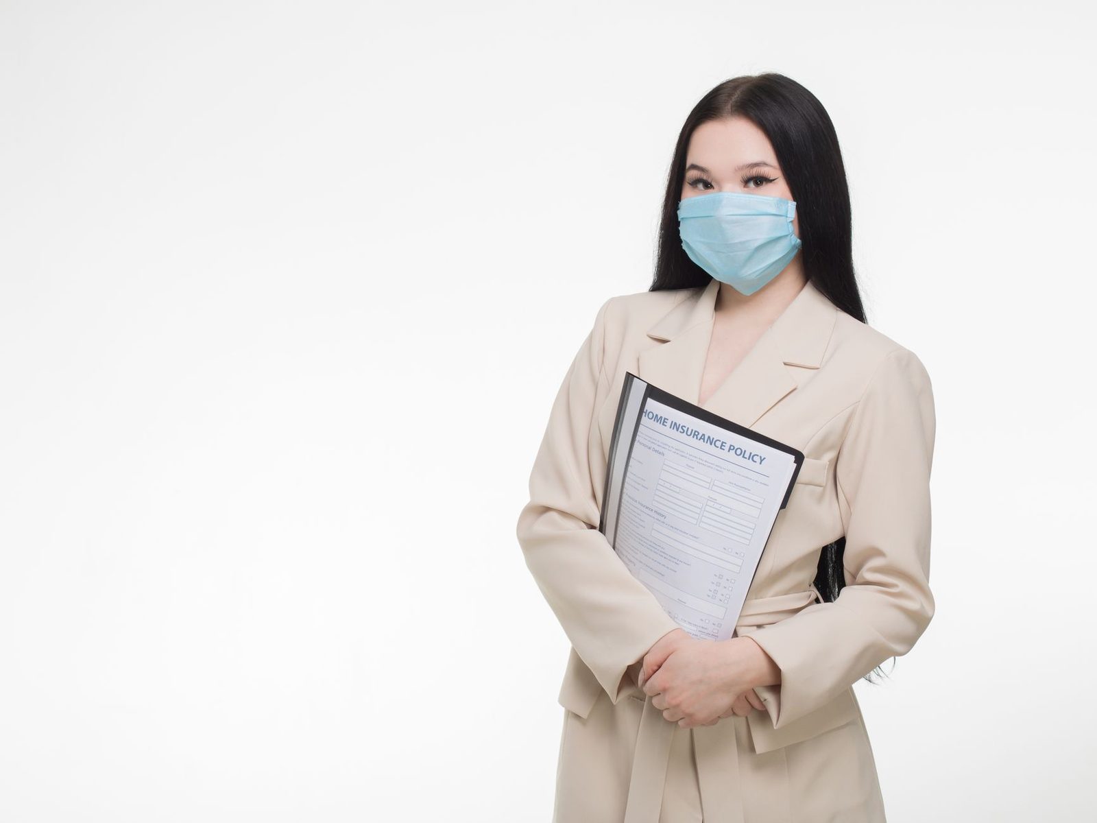 Woman in face mask holding insurance document at desk.